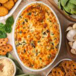 Baked spinach artichoke dip surrounded by baguette slices, pretzels, and ingredients.