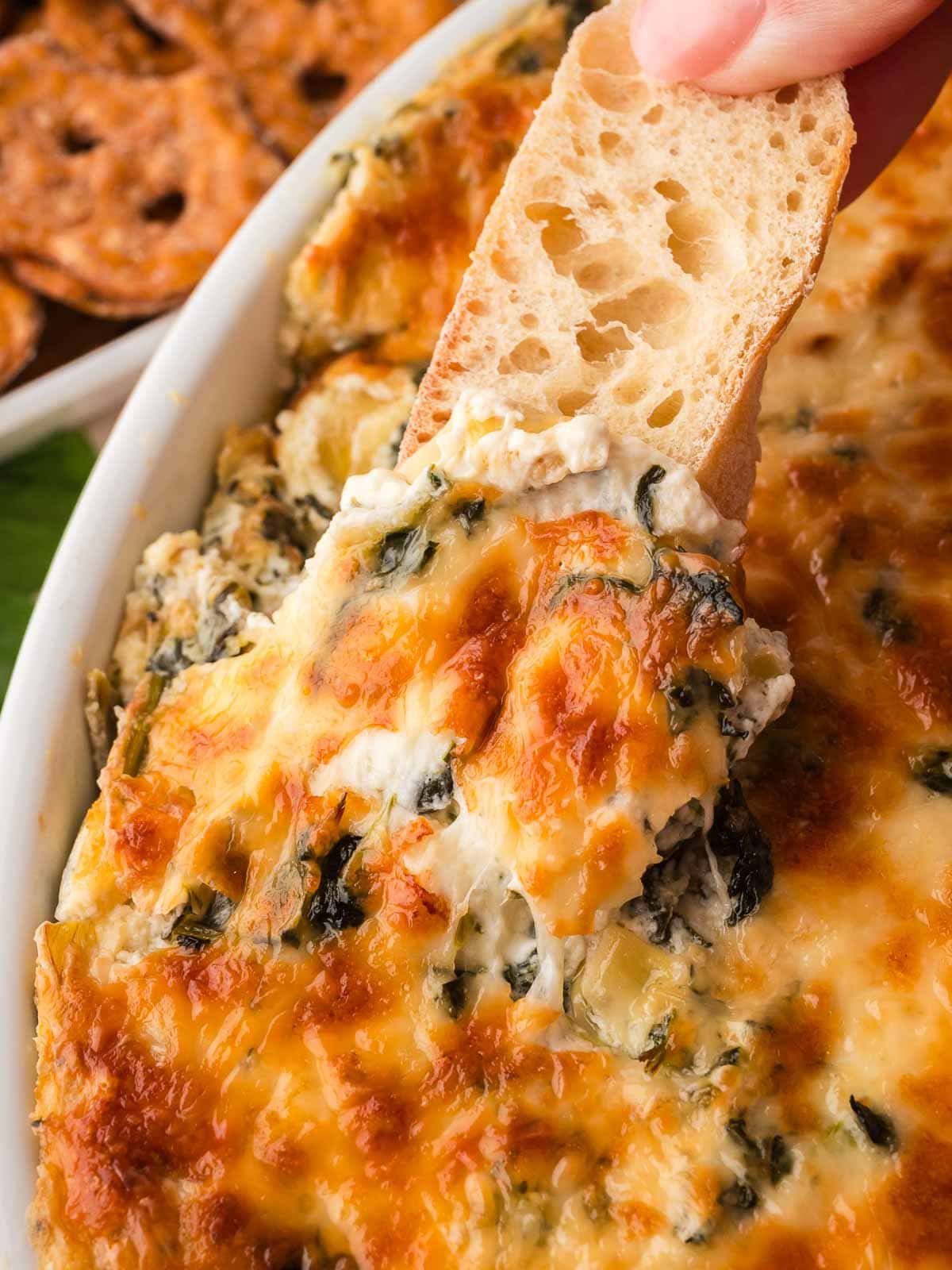 Scoop of hot spinach artichoke dip on a toasted baguette slice lifted from the dish.