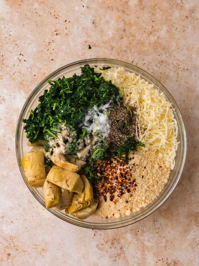Spinach, artichokes, cheeses, and seasonings sitting in a bowl before mixing.