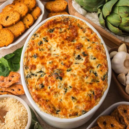 Overhead shot of the dip with bread slices, garlic, artichokes, and cheese around it.