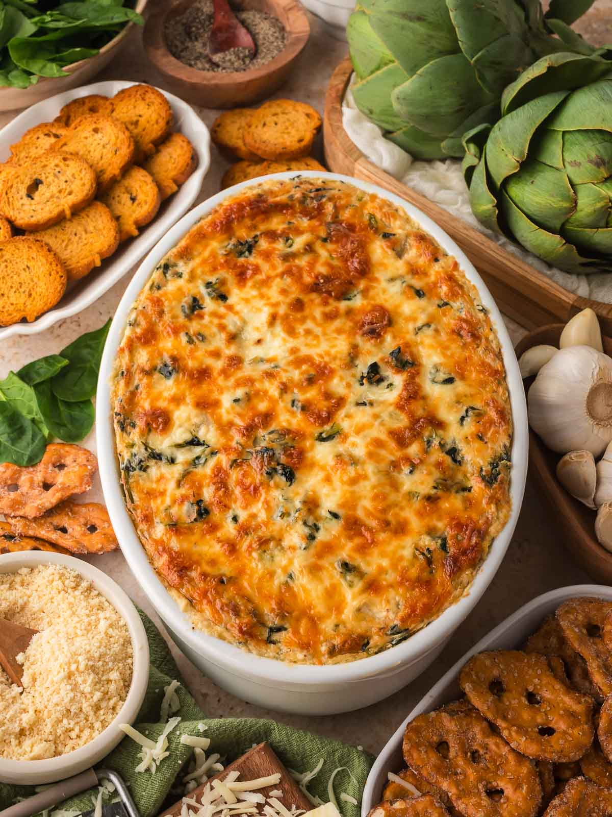 Overhead shot of the dip with bread slices, garlic, artichokes, and cheese around it.