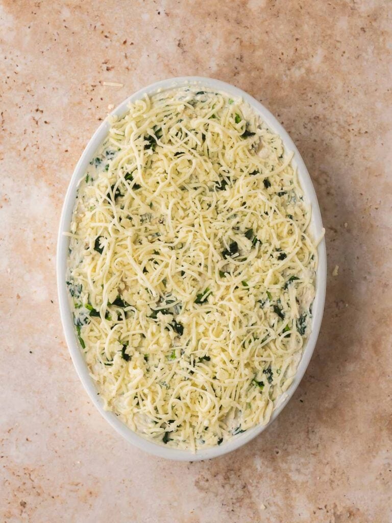 Spinach artichoke dip spread in a baking dish and topped with shredded cheese.