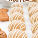 A group of Biscoff truffles on a white surface with cookie crumbs and melted white chocolate in the background.
