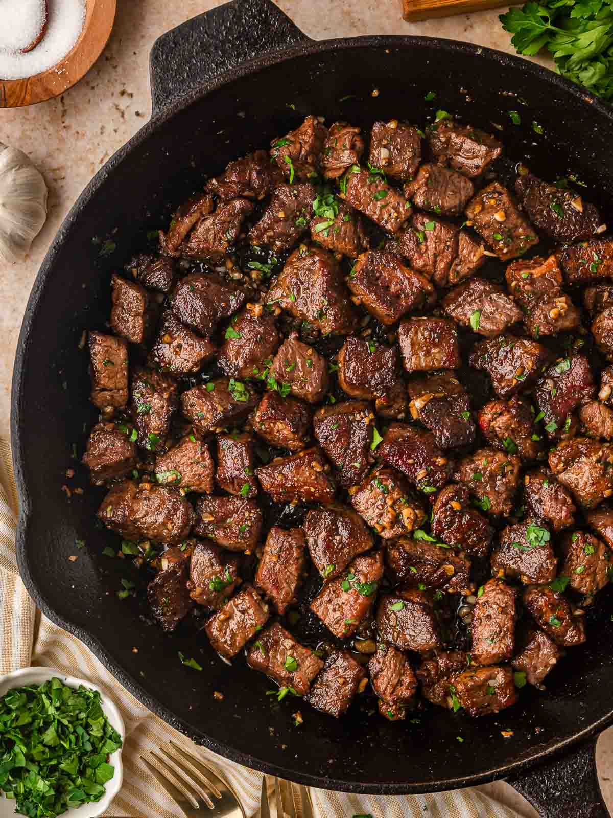 Overhead view of garlic butter steak bites in a cast iron skillet with parsley.
