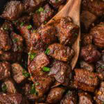 Skillet filled with browned garlic butter steak bites being stirred with a wooden spoon.