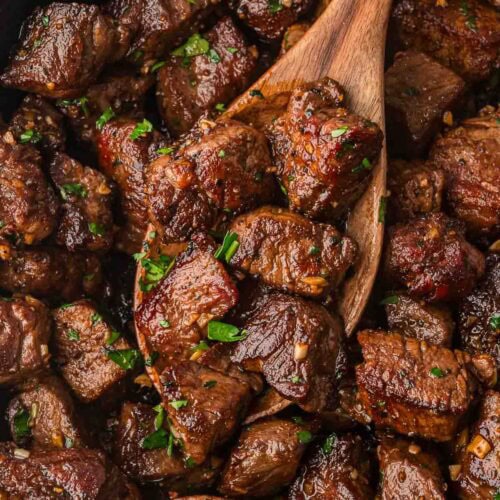 Skillet filled with browned garlic butter steak bites being stirred with a wooden spoon.