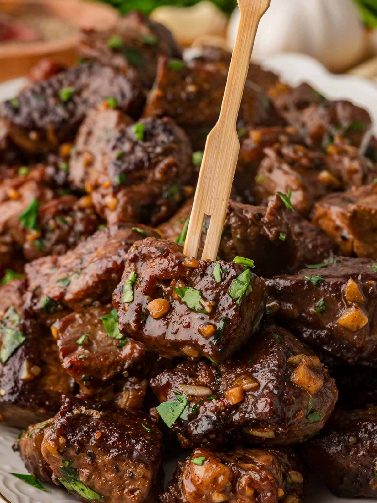 Garlic butter steak bite held up on a small skewer with fresh parsley on top.