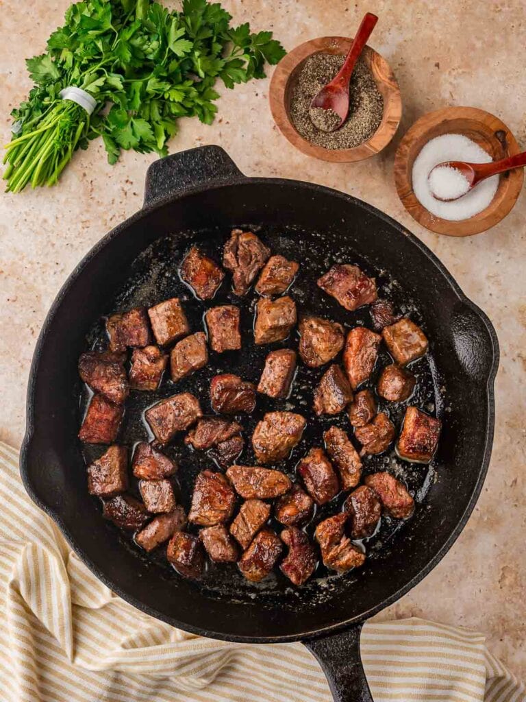 Browned steak bites cooking in a cast iron skillet before adding the garlic.