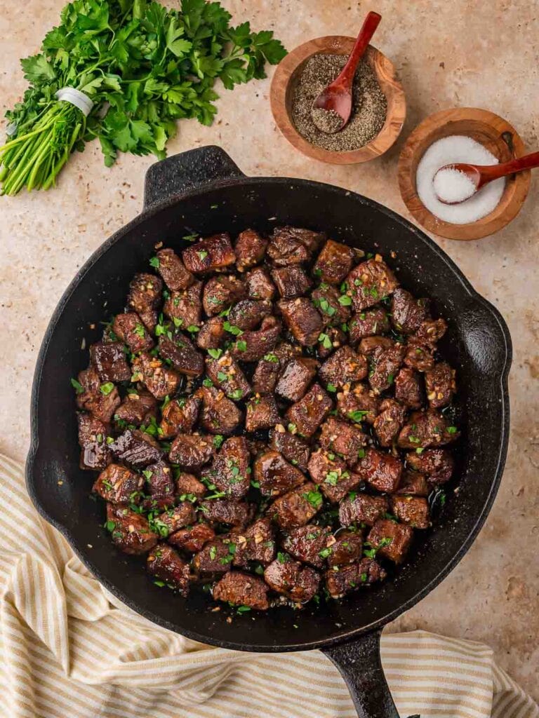 Finished garlic butter steak bites in a cast iron skillet with chopped parsley.