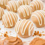 Biscoff truffles on a white surface with cookie butter swirls and crushed cookies in the background.