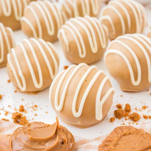 Biscoff truffles on a white surface with cookie butter swirls and crushed cookies in the background.
