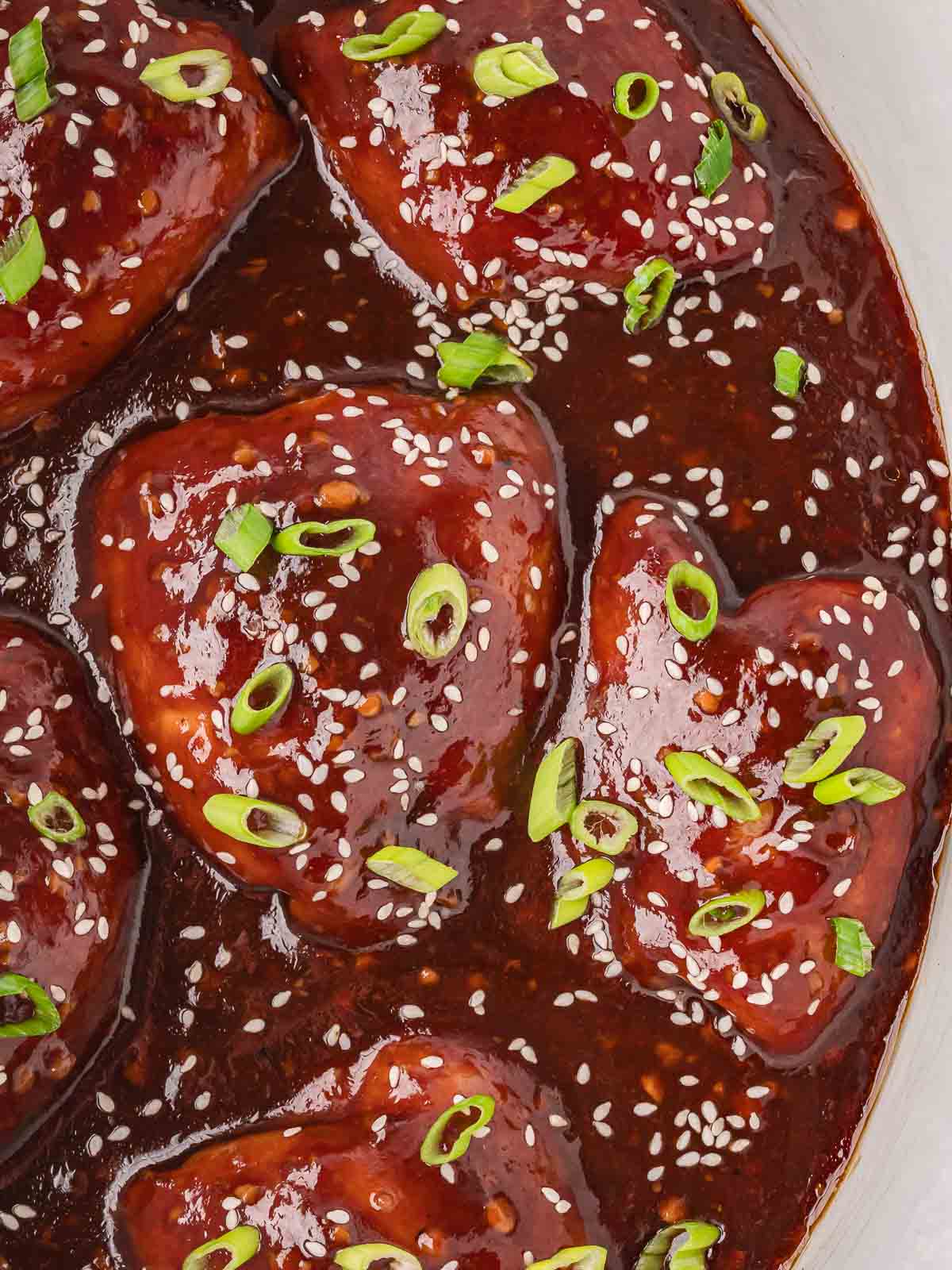 Close-up of tender Crock Pot honey garlic chicken coated in sticky sauce with sesame seeds and green onions.