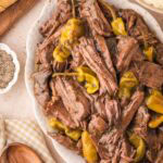 Juicy shredded Mississippi Pot Roast on a white serving platter surrounded by sliced bread and mashed potatoes.