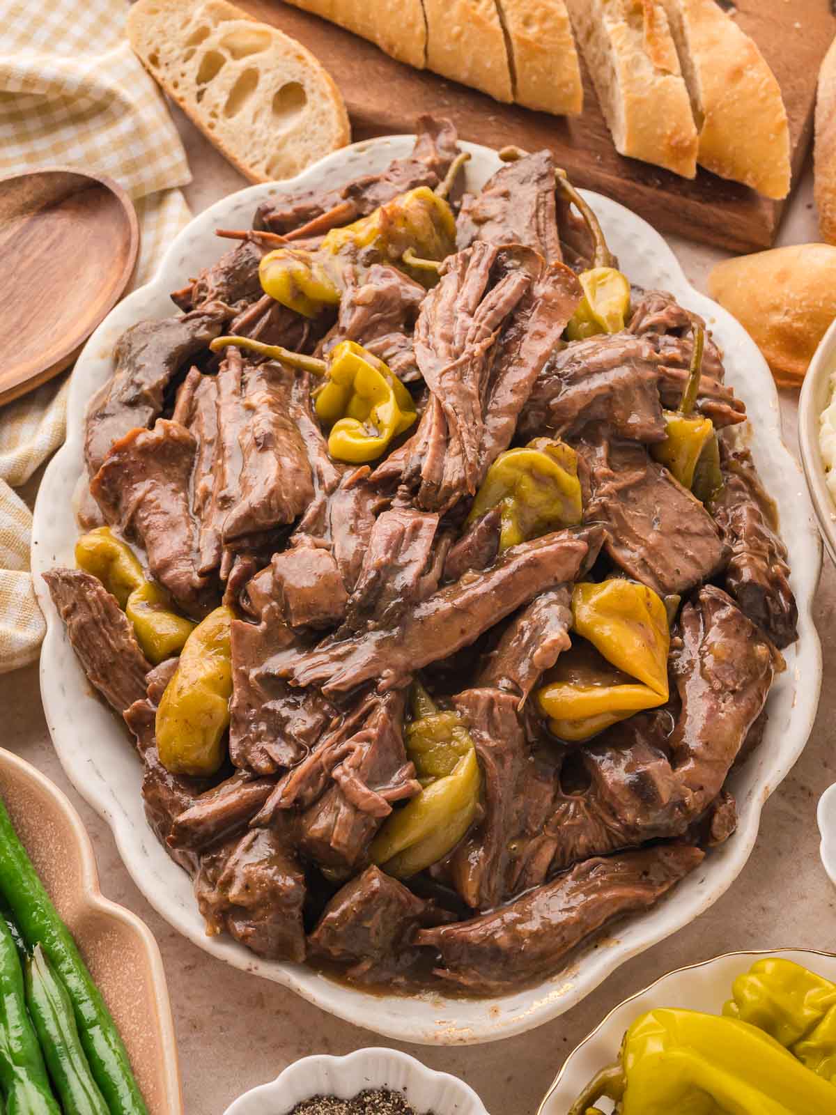Close-up of tender Mississippi Pot Roast served on platter with pepperoncini and rustic bread in the background.