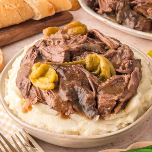 Slow Cooker Mississippi Pot Roast served over creamy mashed potatoes with sliced bread on the side.