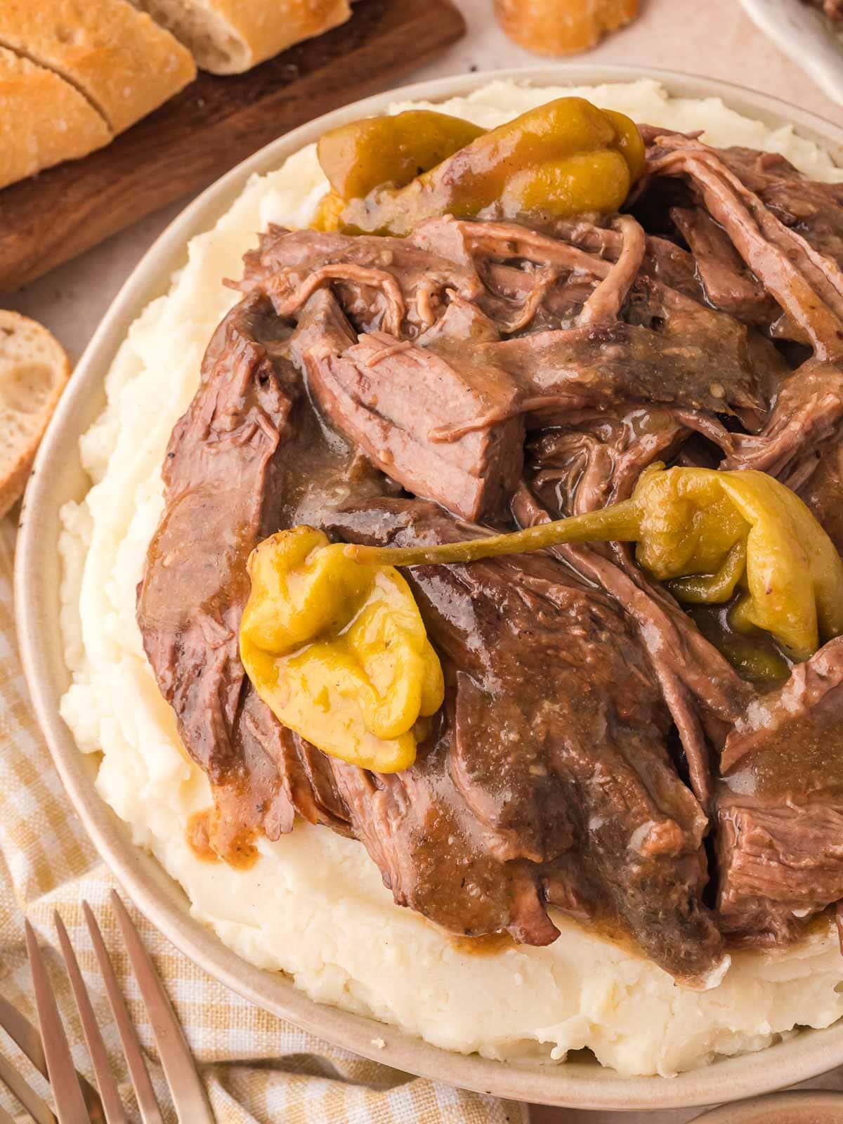 Plate of Slow Cooker Mississippi Pot Roast piled over mashed potatoes with rich sauce and pepperoncini.