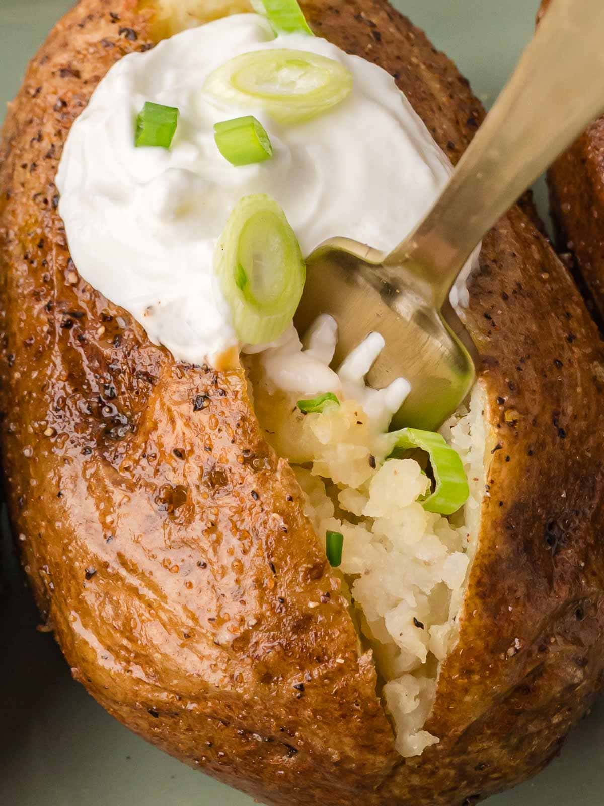 Baked potato split open and fluffed with a fork, topped with sour cream and sliced green onions.