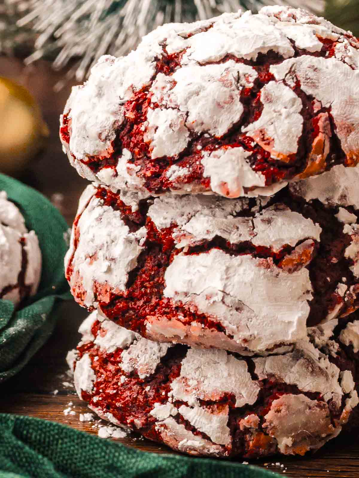 Stack of three red velvet crinkle cookies coated in powdered sugar showing the crinkled tops and rich red centers.