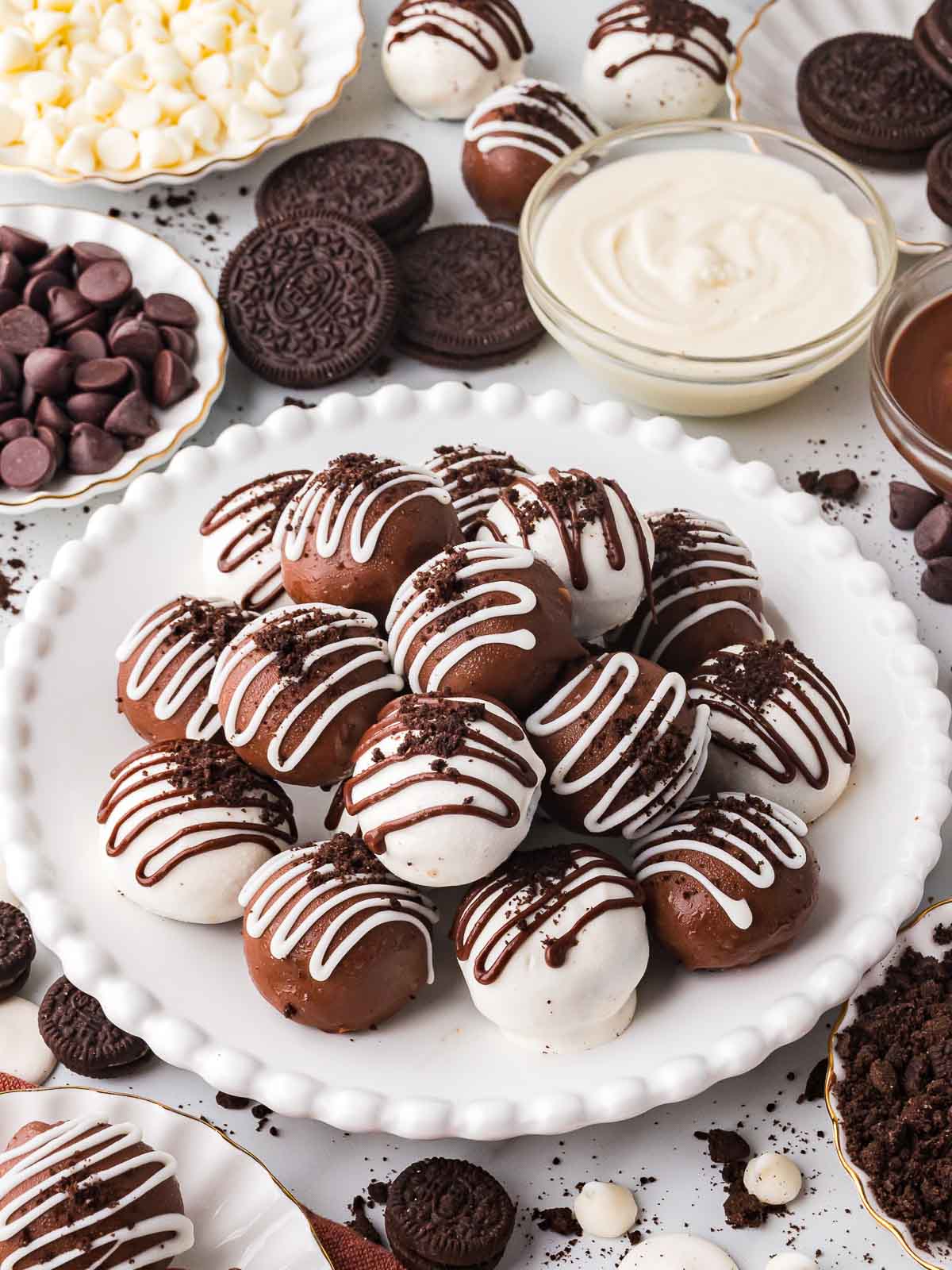 A plate of finished Oreo truffles surrounded by bowls of chocolate chips, melted chocolate, and Oreo cookies.
