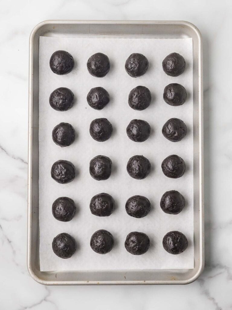 Rolled Oreo truffle balls lined up evenly on a parchment lined baking sheet before freezing.