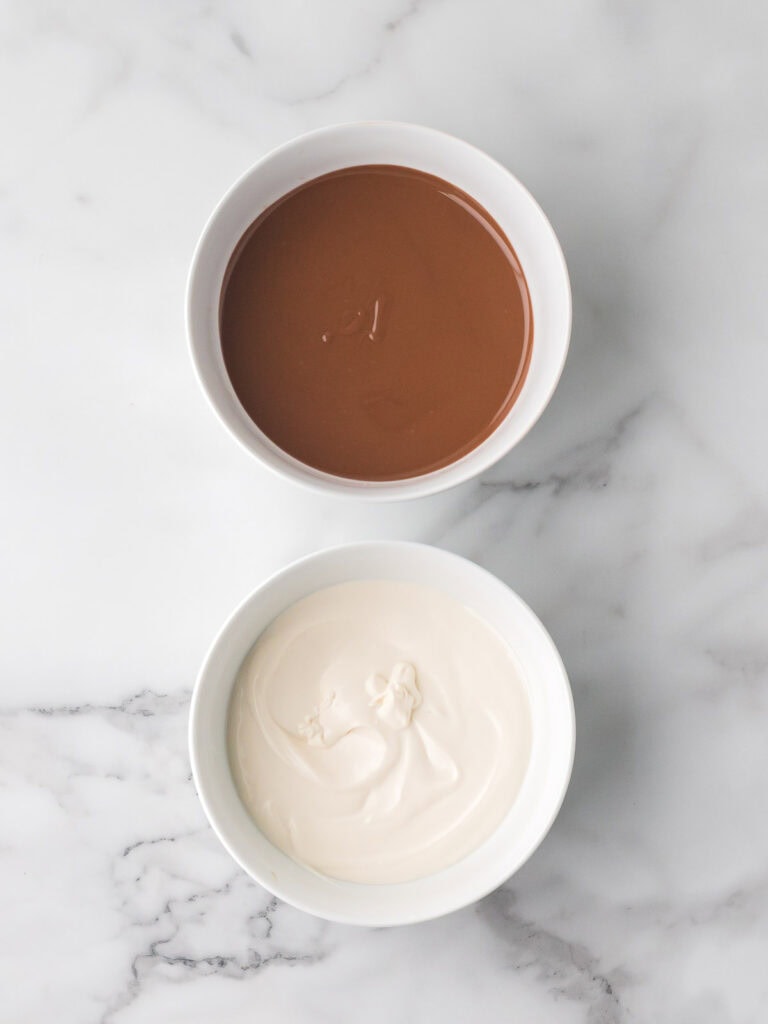 Two bowls of melted chocolate chips, one white and one milk chocolate, smooth and ready for dipping Oreo truffles.