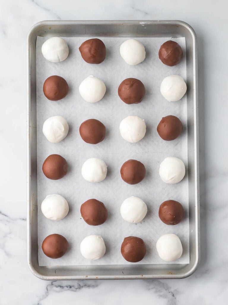 White and milk chocolate coated Oreo truffles setting on a parchment lined baking sheet after dipping.