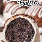 A close up of a bitten Oreo truffle dipped in white chocolate with chocolate drizzle, showing the rich Oreo filling inside.