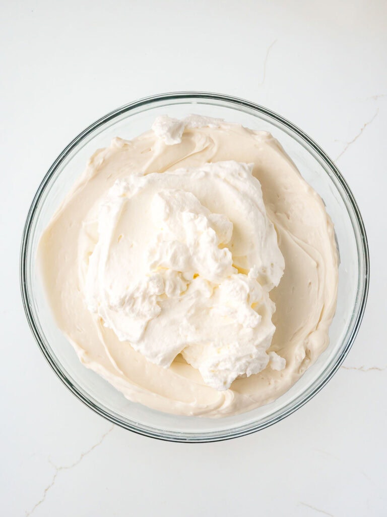 Whipped cream folded into the cheesecake mixture in a glass bowl.