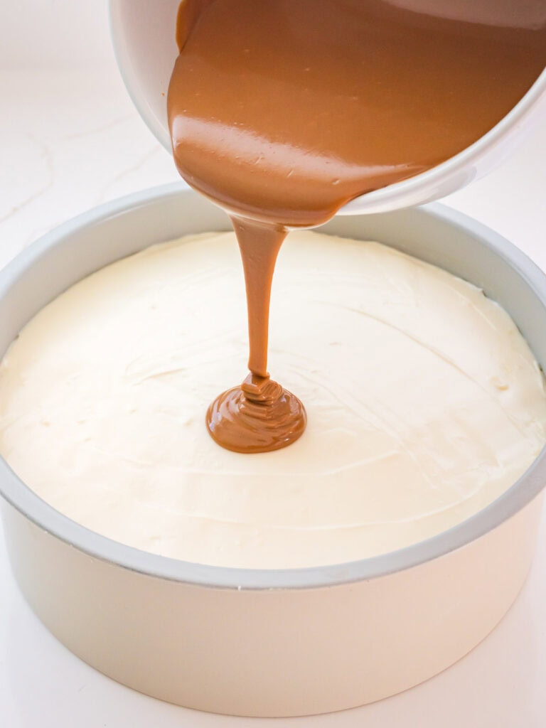 Melted Biscoff cookie butter being poured over the chilled cheesecake filling.