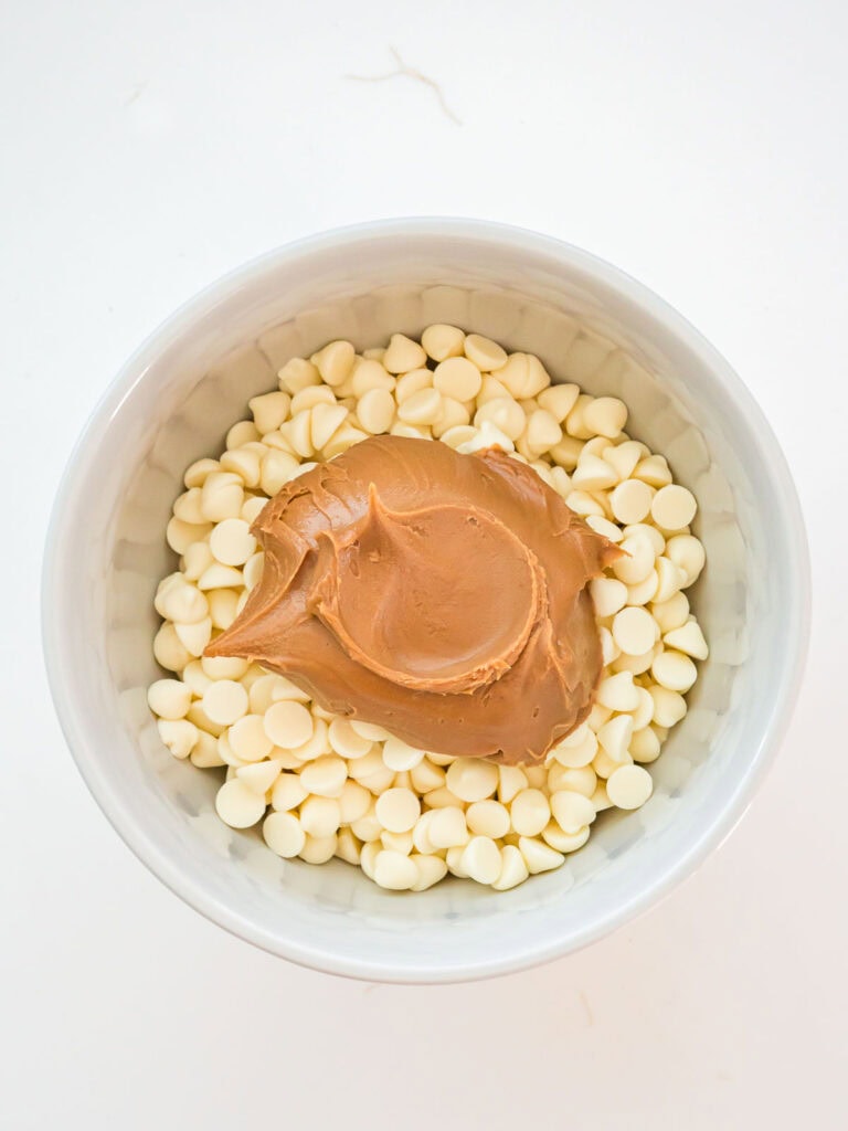 White chocolate chips and a spoonful of Biscoff cookie butter in a white bowl ready to melt for coating truffles.