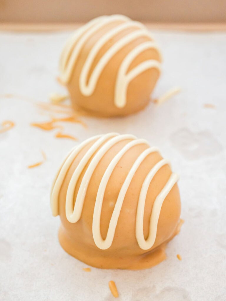Finished Biscoff truffles with white chocolate drizzle setting on parchment paper, ready to chill and serve.