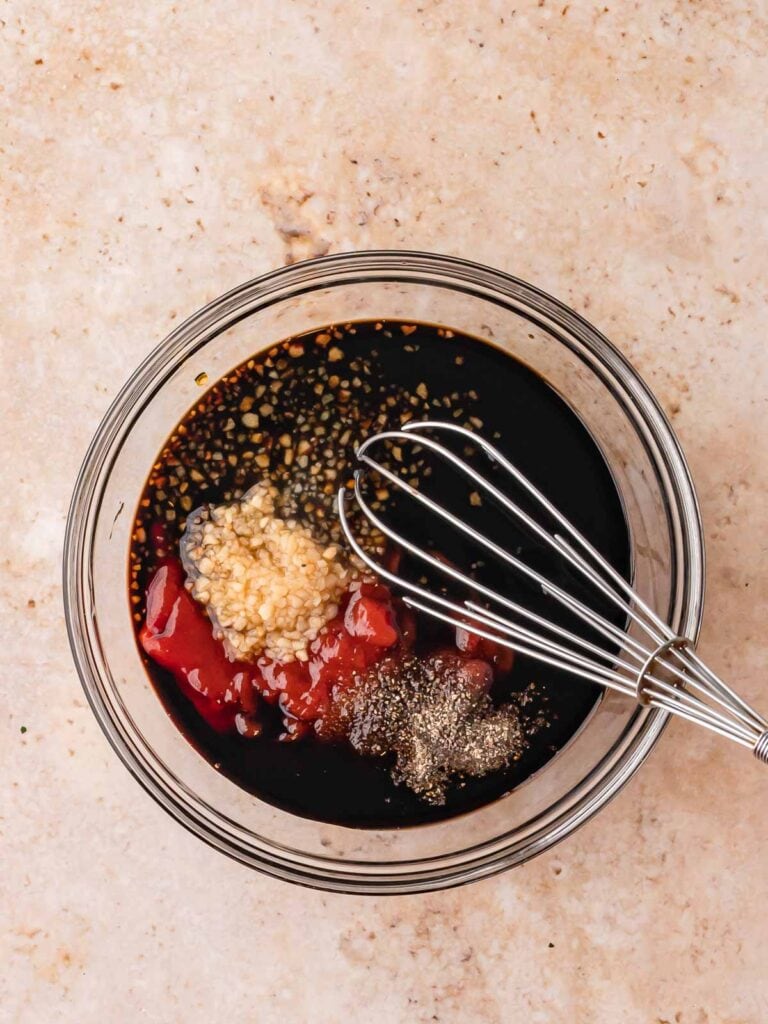 Bowl of honey garlic sauce ingredients — soy sauce, ketchup, minced garlic, and seasonings — being whisked together.
