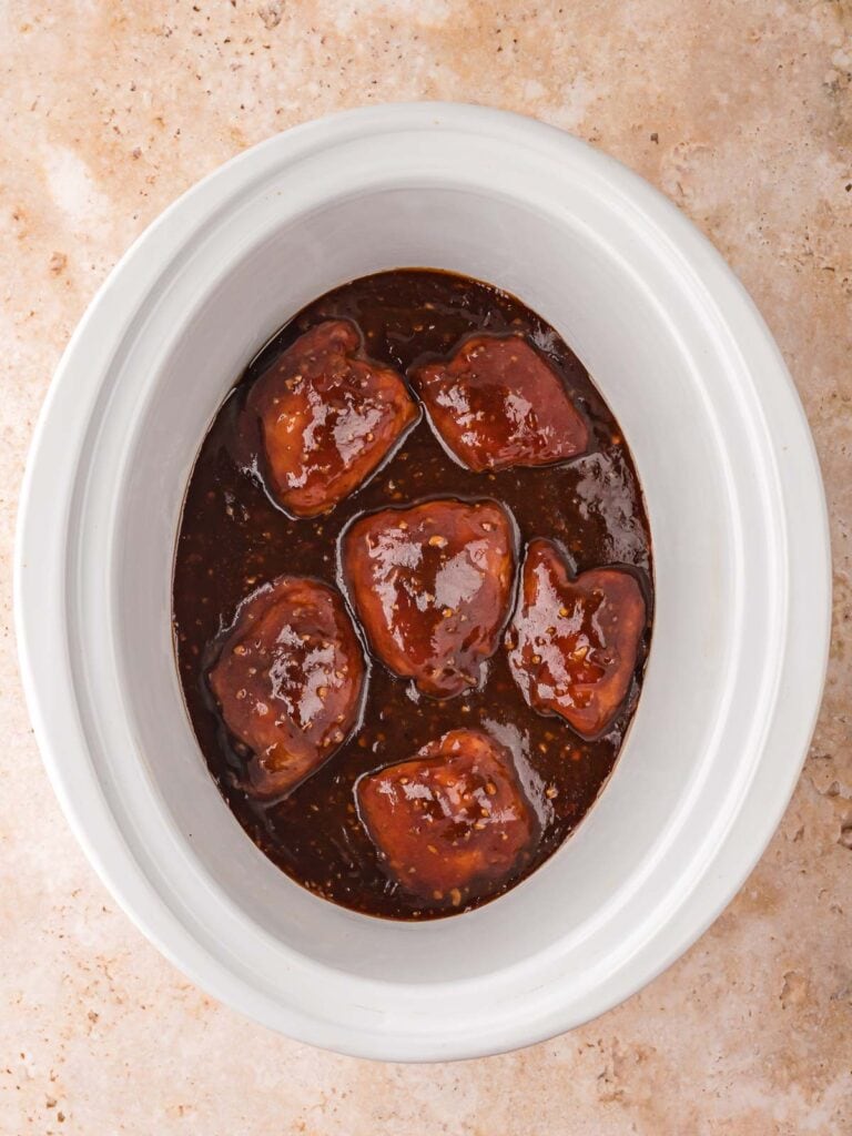 Cooked honey garlic chicken thighs simmering in rich brown sauce inside a white slow cooker.