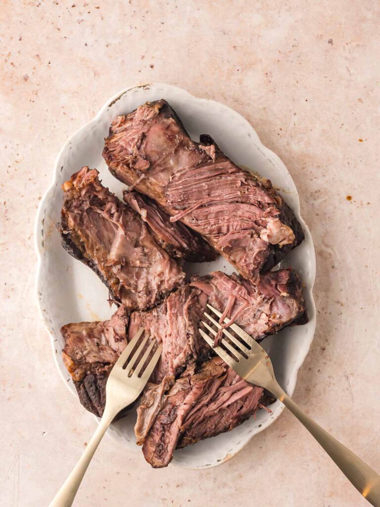 Tender chunks of shredded Mississippi Pot Roast on a white serving dish with two forks ready for pulling apart.