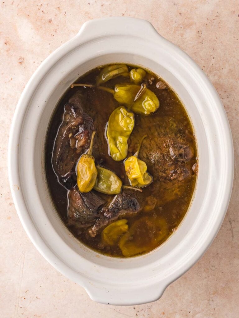 Cooked Mississippi Pot Roast in slow cooker with tender beef and pepperoncini peppers in rich brown sauce.