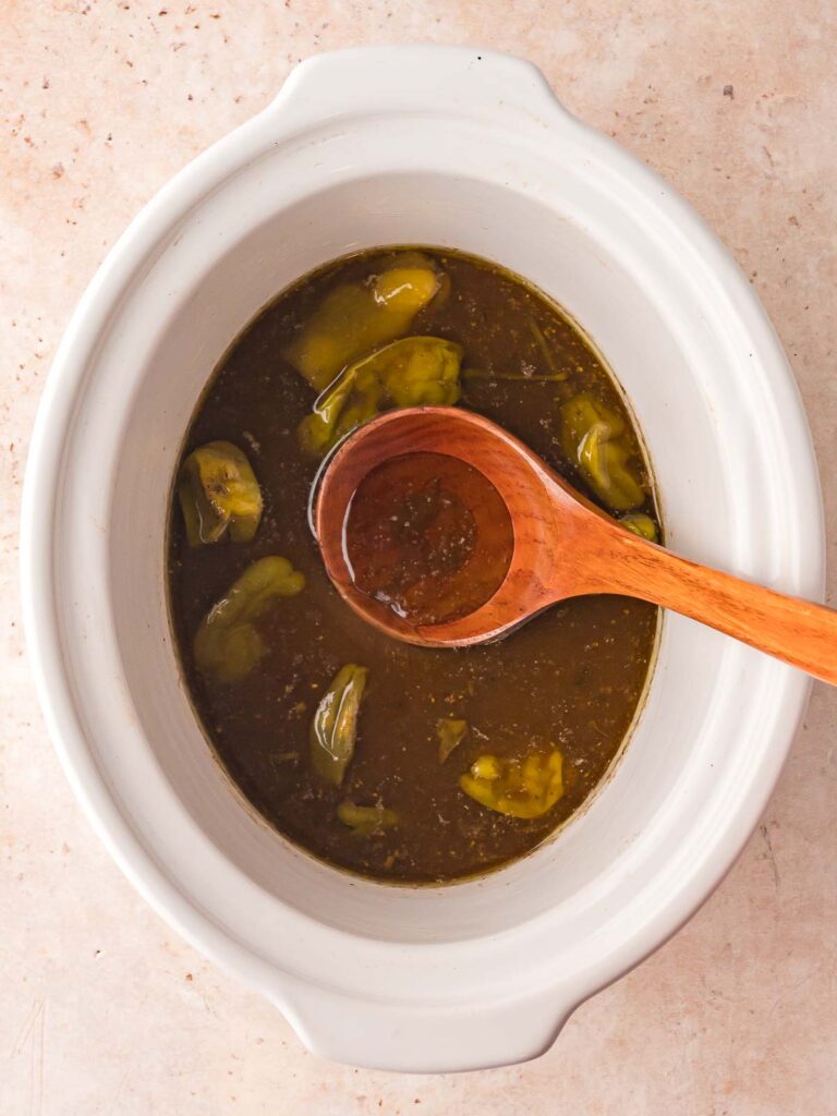 Juicy sauce and cooked pepperoncini peppers left in the slow cooker after removing Mississippi Pot Roast.