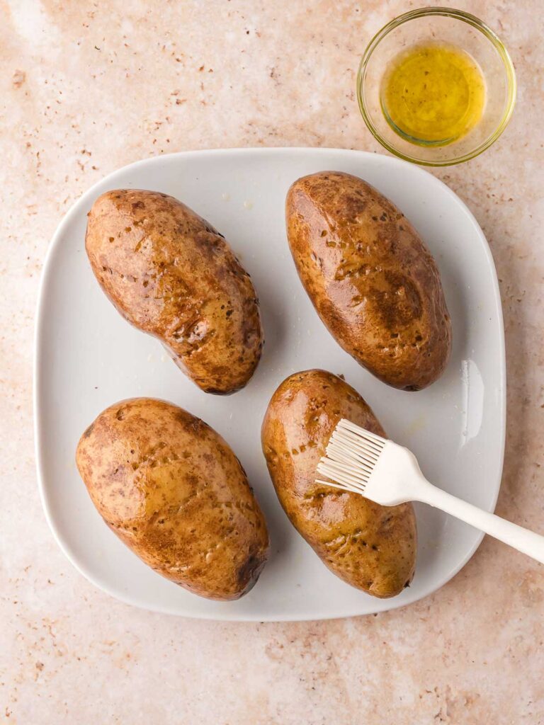 Brushing olive oil over russet potatoes before seasoning.
