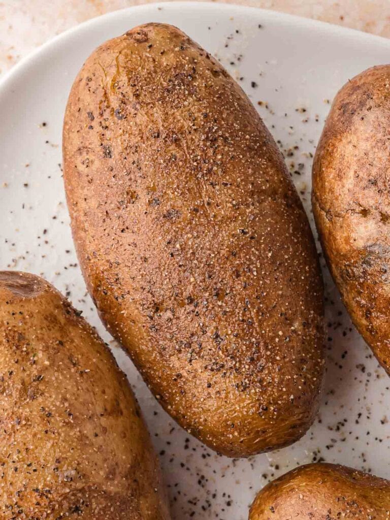Seasoned russet potatoes on a white plate ready for baking