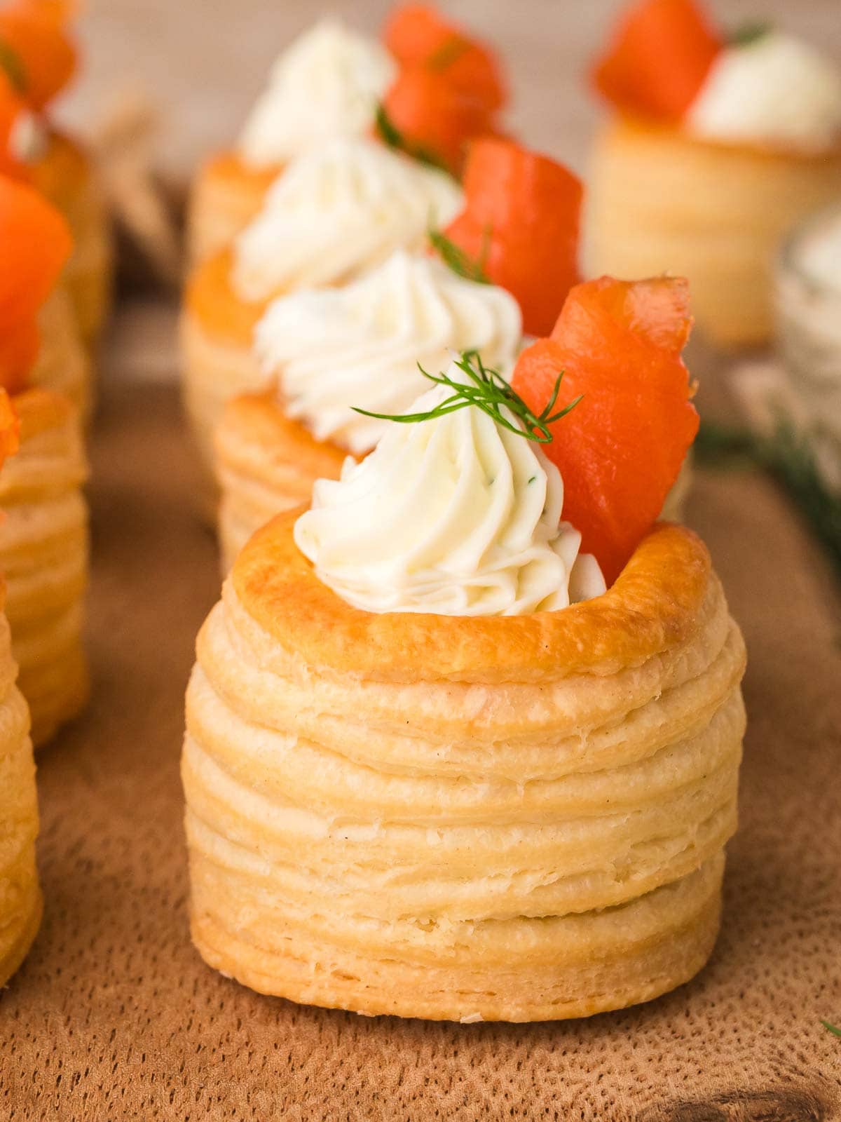 Single smoked salmon puff pastry appetizer with piped cream cheese and dill on a wooden board.