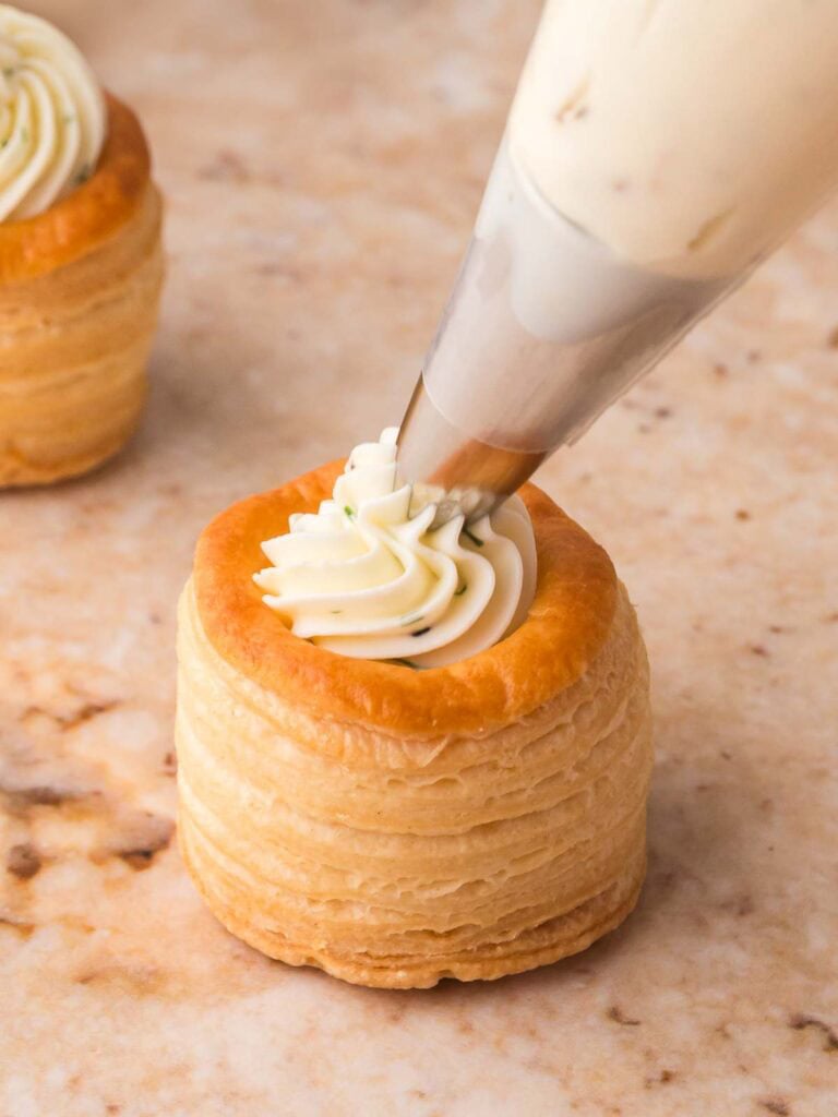 Creamy dill cheese being piped into a mini puff pastry shell.