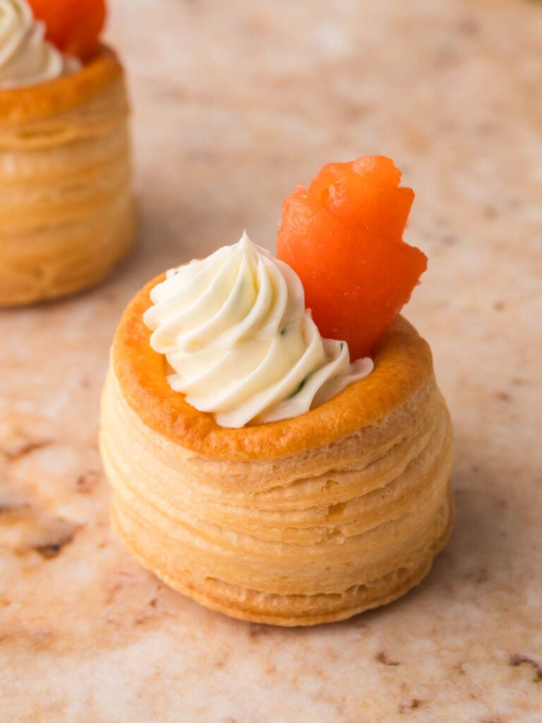 Mini puff pastry shell filled with piped dill cream cheese and topped with a rolled piece of smoked salmon.
