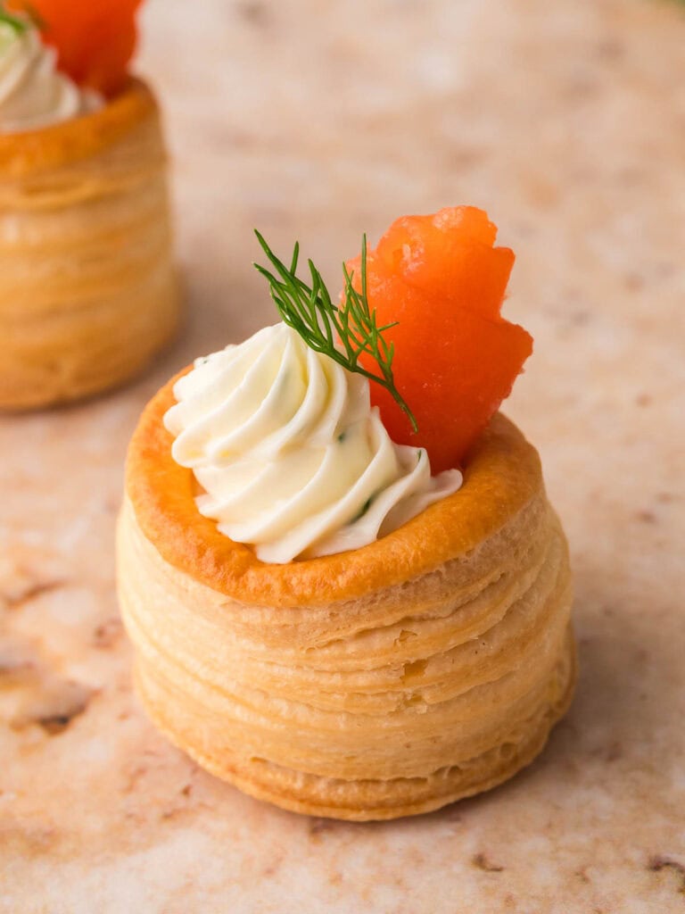 Close view of a puff pastry shell filled with dill cream cheese and a small roll of smoked salmon on top with fresh dill.