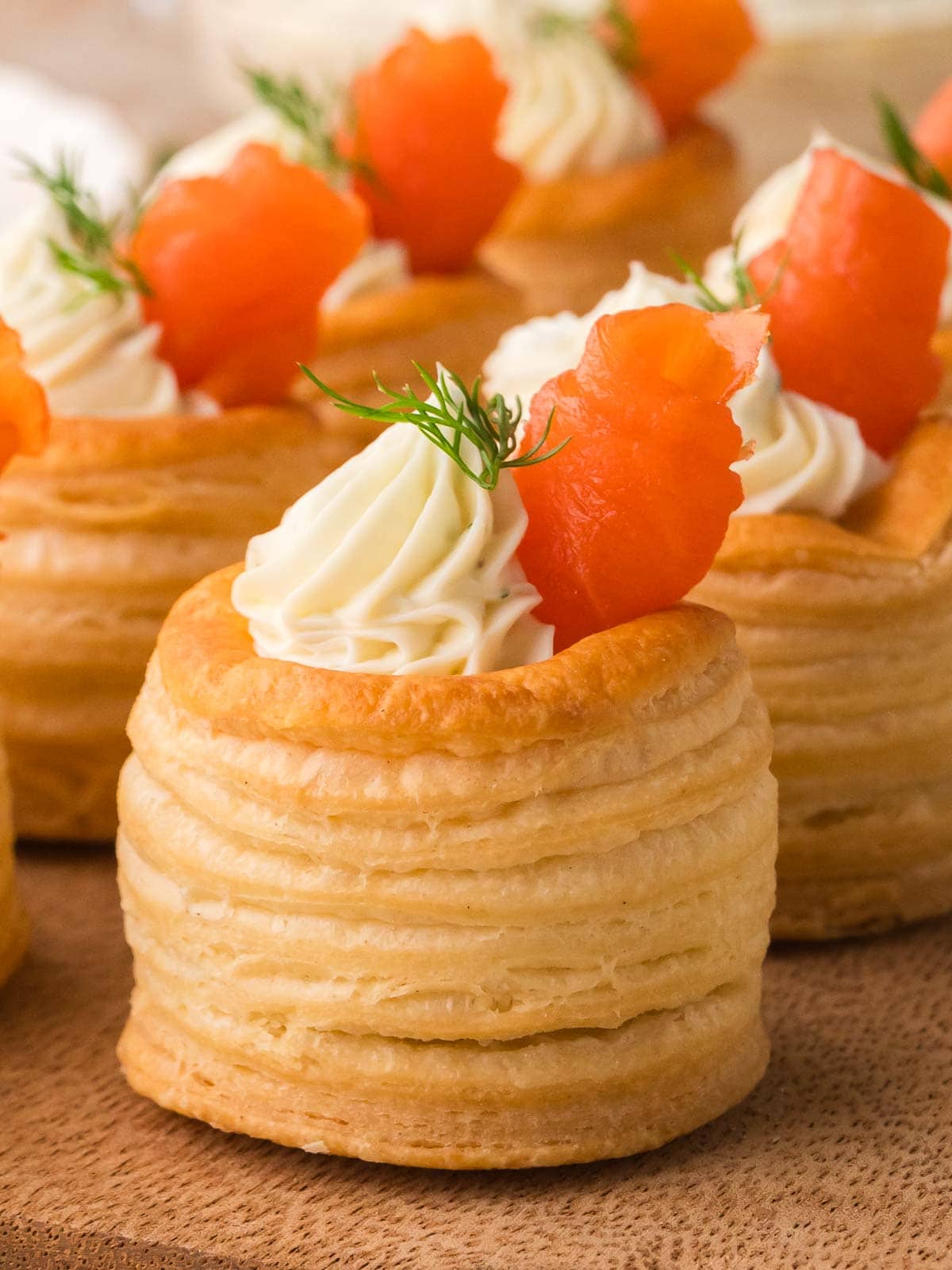 Finished smoked salmon appetizers in puff pastry shells topped with dill cream cheese and fresh dill.