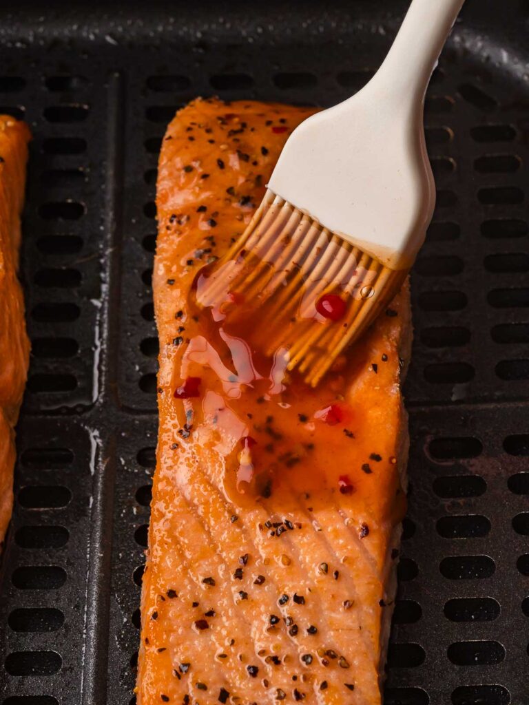 A close up of sweet chili glaze being brushed onto a salmon fillet in the air fryer for Air Fryer Sweet Chili Salmon.