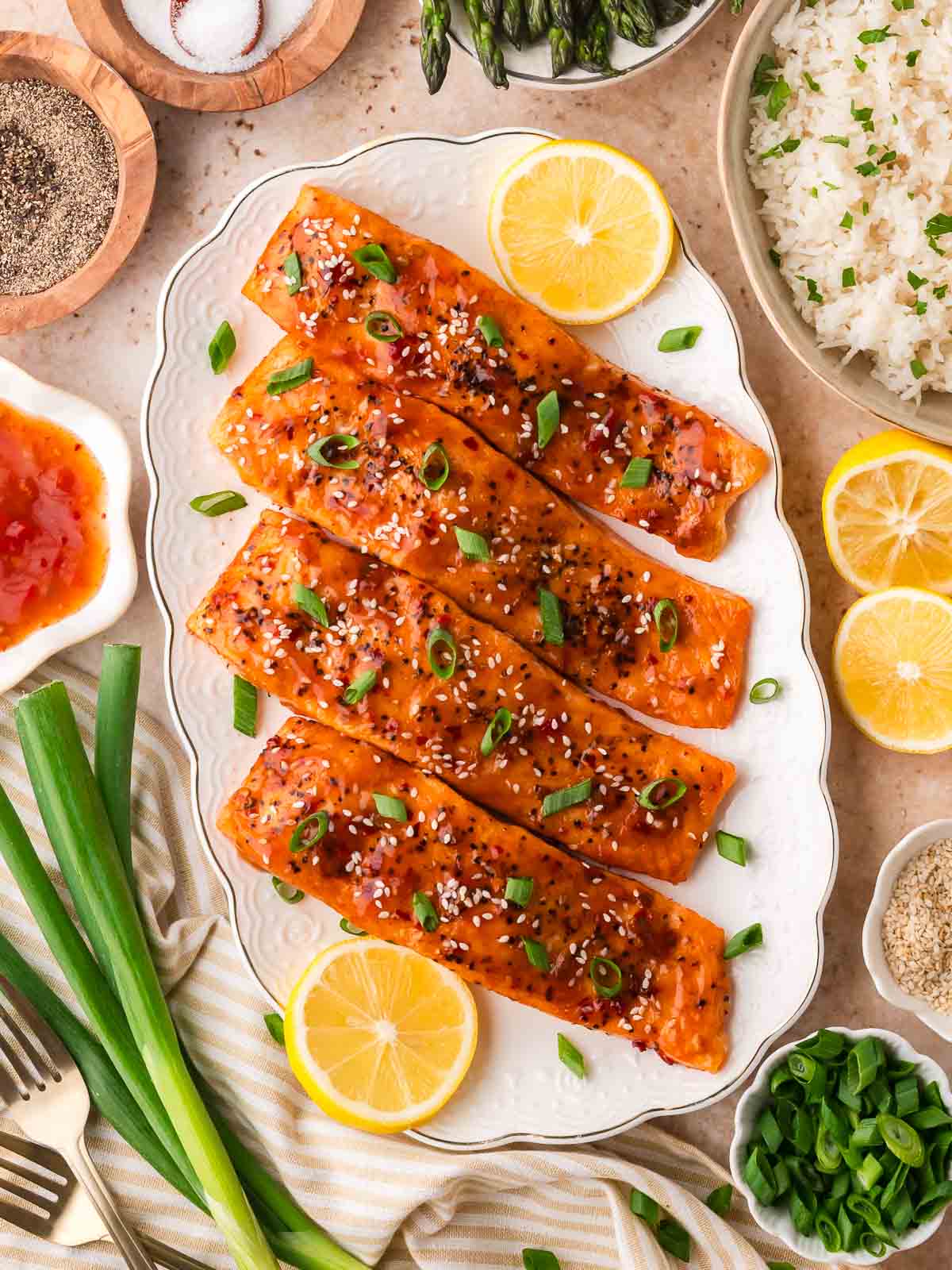 Air Fryer Sweet Chili Salmon arranged on a white serving plate with lemon slices, green onions, rice, and asparagus set around the dish.