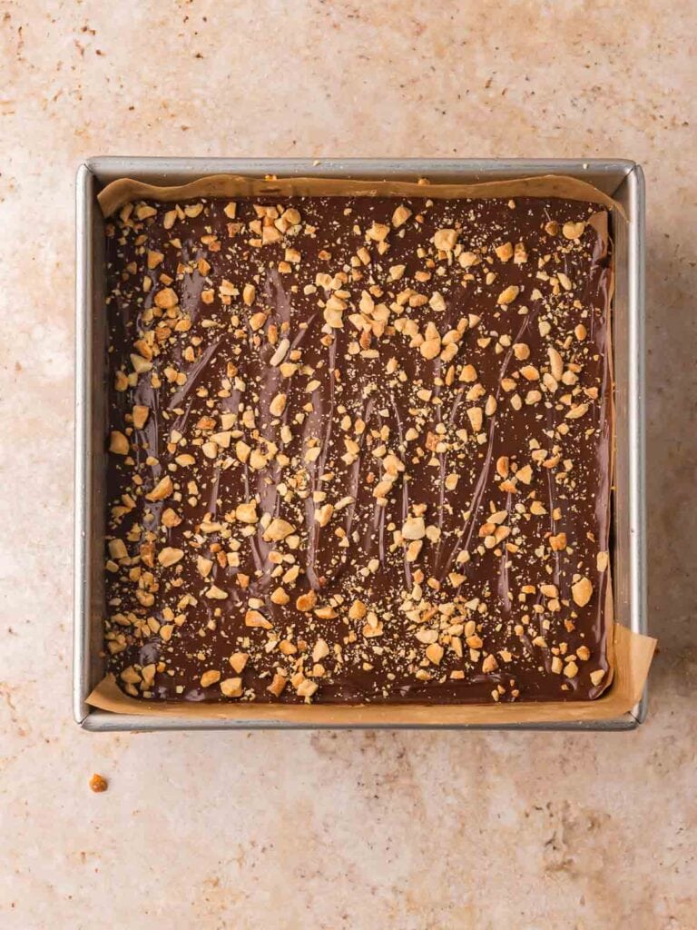 Chocolate peanut butter protein bars topped with crushed peanuts after the chocolate layer has been spread.