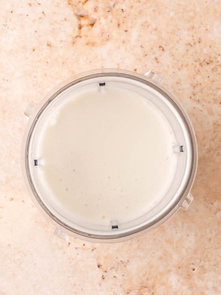 Smooth blended creamy mixture in a blender cup for adding to chicken noodle soup, photographed on a light stone background.