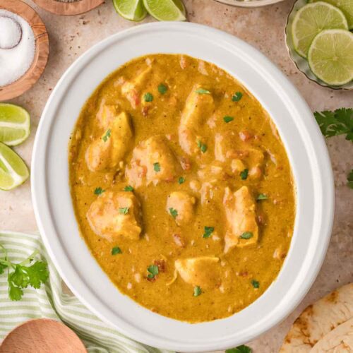 Crockpot filled with coconut chicken curry surrounded by bowls of rice, lime wedges, and fresh cilantro.