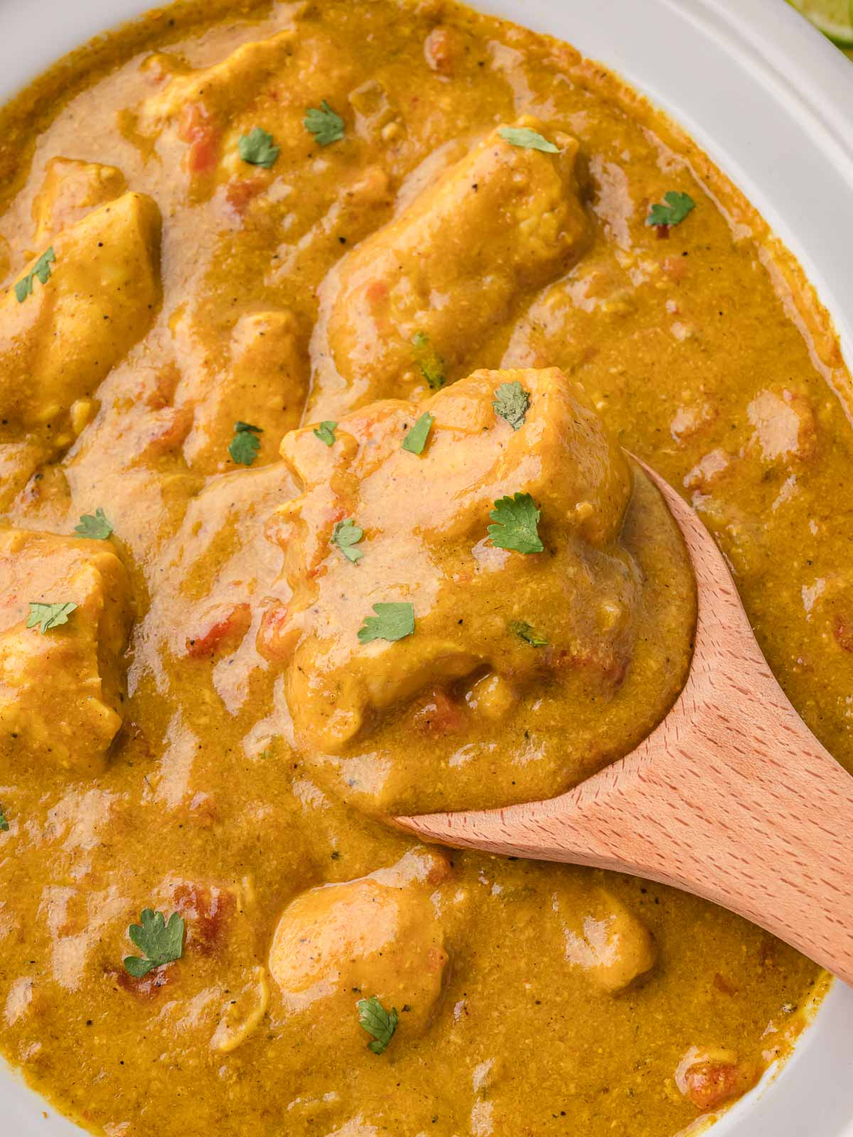 Creamy slow cooker chicken curry being scooped with a wooden spoon, showing tender chicken pieces.