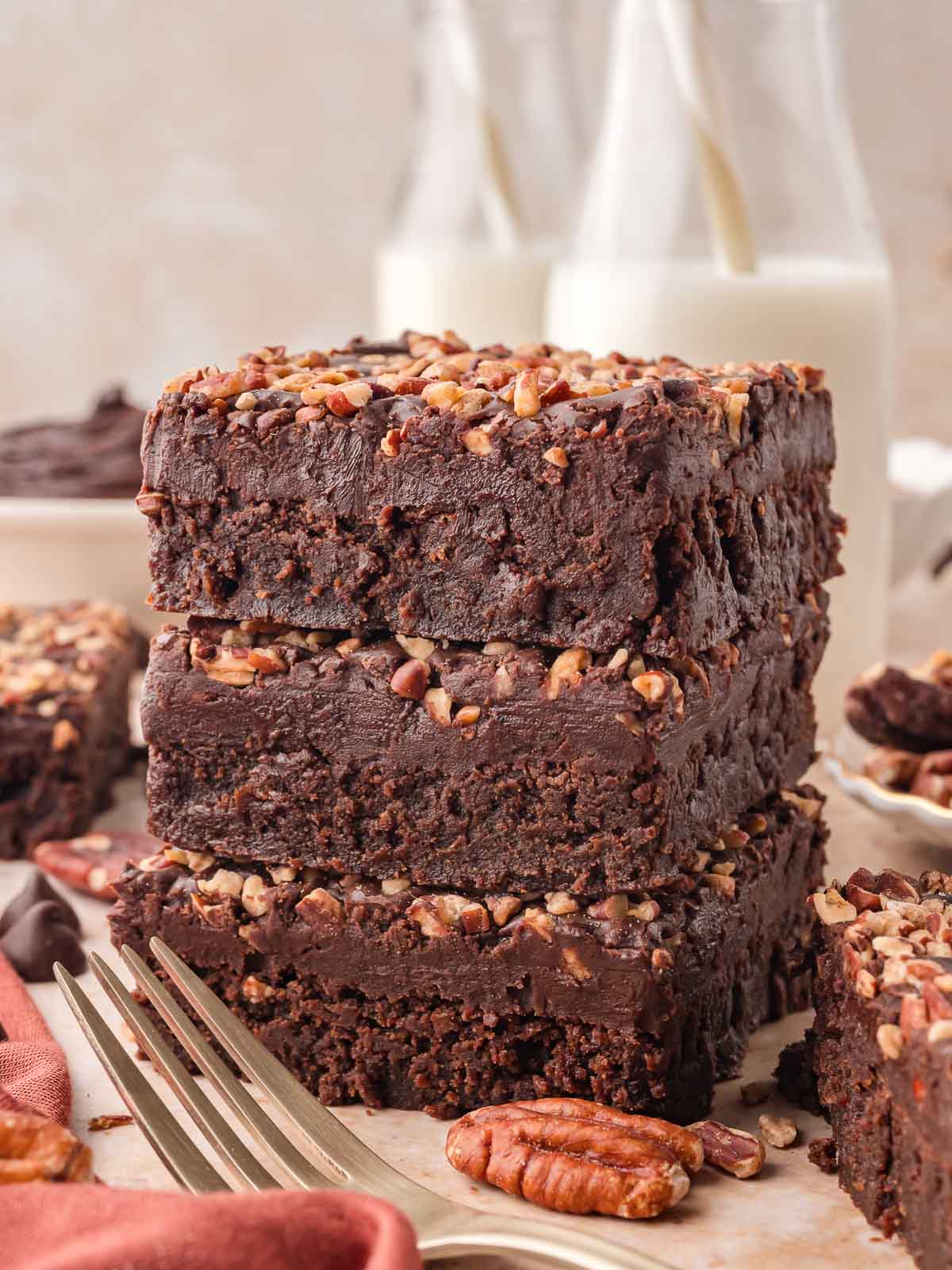 Stack of thick Texas Sheet Cake squares with glossy chocolate frosting and pecans, highlighting the soft, fudgy layers next to bottles of milk.